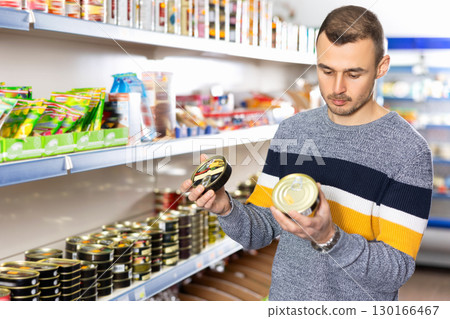 In Russian goods store, man choose canned sprats in oil 130166467
