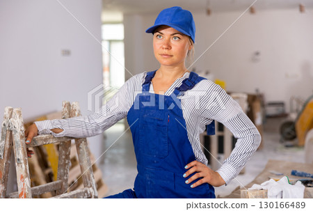 Female builder in blue overalls standing at construction site indoors 130166489