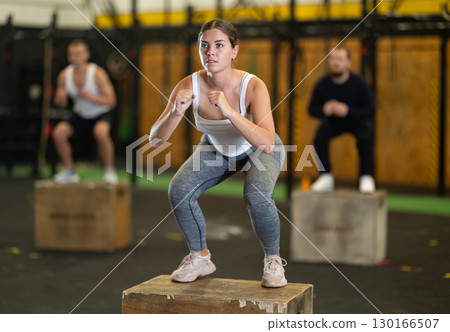 Sportive young girl squatting on box during crossfit workout 130166507