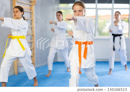 Team of teenage girls in kimonos uses new fighting techniques during karate lessons in gym 130166523