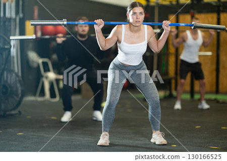 Young woman performing exercises with barbell during intense training 130166525