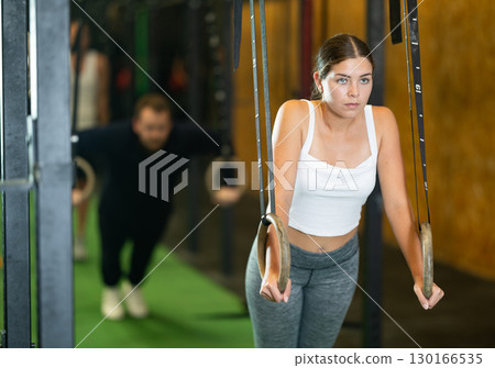 Sportive young girl working out with gymnastic rings in gym during crossfit workout 130166535