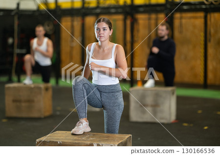 Focused girl stepping up on box during cross training at gym Focused girl stepping up on box during cross training at gym 130166536
