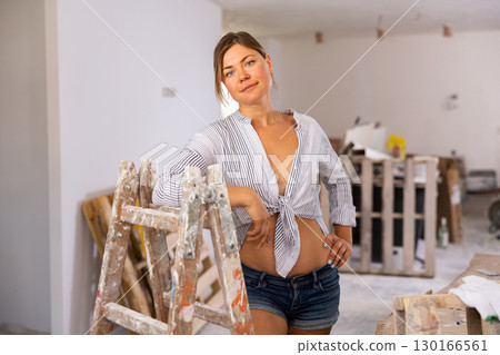 Sensual woman in shorts and unbuttoned male shirt posing in room under reconstruction 130166561