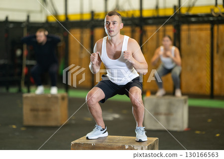 Sportive young guy squatting on box during crossfit workout 130166563