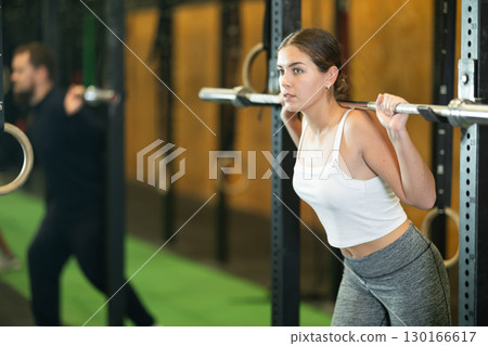 Fit girl doing exercises with barbell during group workout 130166617
