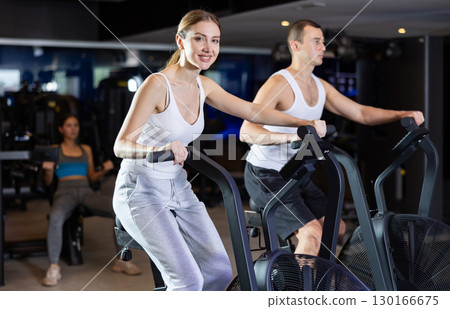 Sportive young couple doing air bike exercises in well-equipped gym 130166675