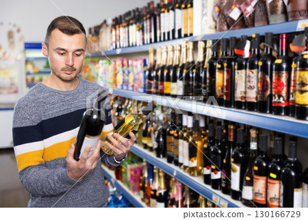 In Russian goods store, man choose bottle of wine 130166729