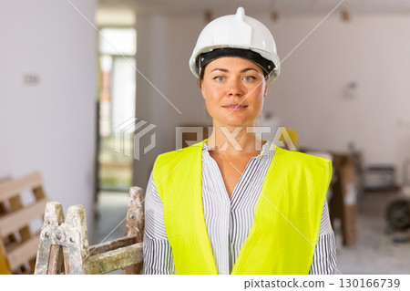 Confident female builder in vest and hard hat standing at construction site Confident female builder in vest and hard hat standing at construction site 130166739