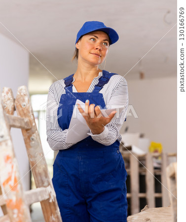 Cheerful young woman builder checking project documentation 130166769