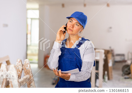 Female worker in blue overall discussing repair plan on mobile phone Female worker in blue overall discussing repair plan on mobile phone 130166815
