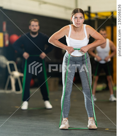 Determined young girl working out with resistance band in gym 130166836