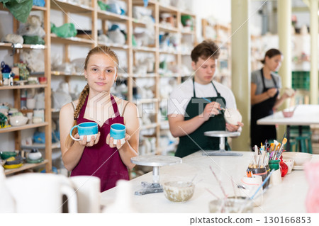 Teenage girl posing with ceramic cup in ceramic workshop 130166853