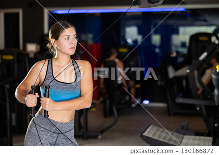 Active athlete young woman during exercises on crossover exercise machine with loops and weighting 130166872