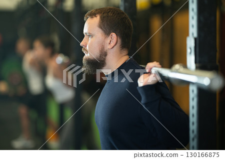 Bearded man doing exercises with barbell during group workout 130166875