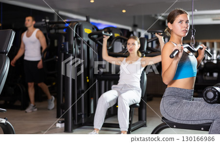 Slender athletic girl work out muscles of arms and shoulders on simulator in gym of fitness club 130166986