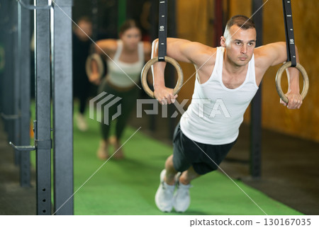 Man performing chest push-ups with gymnastic rings during workout in gym 130167035