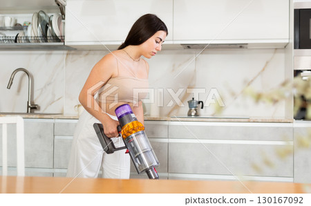 Young woman vacuuming floor in kitchen at home 130167092
