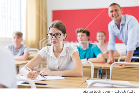 Smiling teenage schoolgirl in glasses sitting in classroom during lesson 130167125