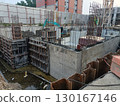 Construction site shows concrete walls and steel reinforcement bars being installed, with workers and machinery actively working building 130167146