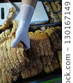 Person wearing white glove handling fried pork belly food stall, with crispy, golden brown pork pieces displayed tray, ready for sale or serving 130167149