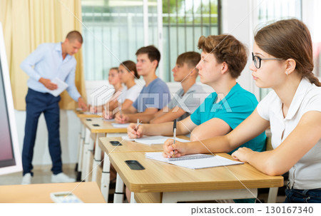 Teenage schoolgirl in glasses writing in workbook during lesson 130167340