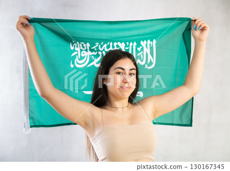Happy young woman with flag of Saudi Arabia against unicoloured background Happy young woman with flag of Saudi Arabia against unicoloured background 130167345