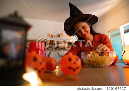 Halloween Fun: Young Woman Preparing Snacks in Witch Hat Halloween Fun: Young Woman Preparing Snacks in Witch Hat 130167617