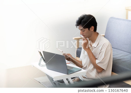 Focused Work. Young man studying with laptop and tablet at home. Focused Work. Young man studying with laptop and tablet at home. 130167640