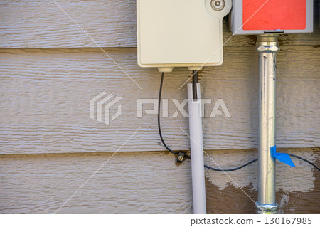 Utility box mounted on wooden exterior with cables connecting to nearby pipe 130167985