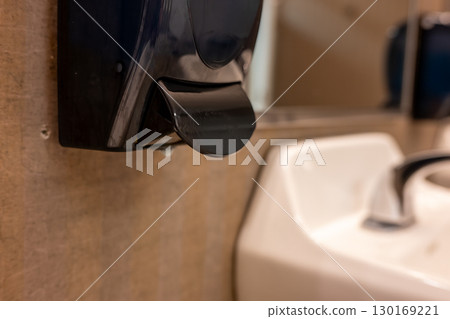 Soap dispenser mounted on wall next to sink in a modern restroom facility Soap dispenser mounted on wall next to sink in a modern restroom facility 130169221