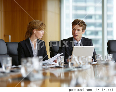 Two business professionals discussing documents in a modern office meeting 130169551