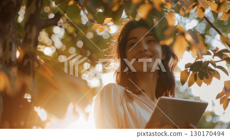 woman reading tablet under tree sunlight 130170494