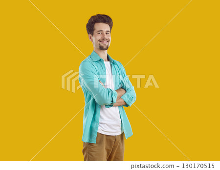 Smiling young man standing with hands crossed on yellow background 130170515