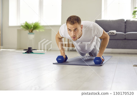 Portrait of serious sports man who does sports at home and trains muscles using dumbbells. Portrait of serious sports man who does sports at home and trains muscles using dumbbells. 130170520