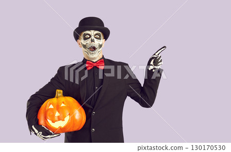 Shocked man dressed in Day of the Dead costume points his finger to side on light lilac background Shocked man dressed in Day of the Dead costume points his finger to side on light lilac background 130170530