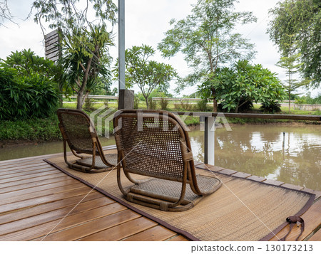 Rattan Chair on Mat on Wooden Deck by Small Pond. 130173213