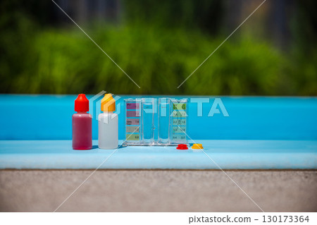 Pool water test kit with chemical dropper bottles and color comparator, used for swimming pool maintenance, placed on the edge in sunlight. 130173364