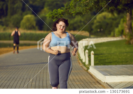 Purposeful overweight Caucasian woman doing sports and running in morning in park. 130173691