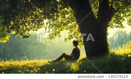 A peaceful moment of a person sitting quietly under a large tree with no devices, embracing nature. Ideal for wellness, mindfulness, and slow living themes. 130174124