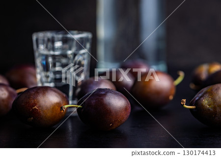 Plums and distilled alcohol on black table. Plum brandy shot. 130174413
