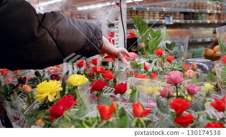 Shopper chooses a bunch of vibrant roses from the floral section of a supermarket, enhancing the shopping experience with their beauty and fragrance 130174538