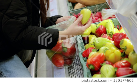 Customer choosing vibrant bell peppers from a grocery store display and packing a plastic bag with fresh produce for a nutritious diet 130174605