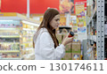 Young woman carefully reviewing product details on a jar of sauce, making thoughtful decisions about her purchases in a well lit supermarket 130174611