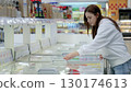 Young woman opening freezer in supermarket, choosing frozen products while shopping for groceries in refrigerated section 130174613