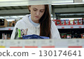 Young woman carefully choosing frozen items in a well lit supermarket, inspecting food packages in the freezer section 130174641