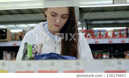 Young woman carefully choosing frozen items in a well lit supermarket, inspecting food packages in the freezer section 130174641