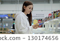 Young woman browsing groceries in a supermarket, carefully reading product details on packaging in the refrigerated section of the store 130174656