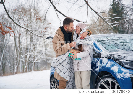 With warm towel. Happy couple having a walk in winter forest. Blue car is parked With warm towel. Happy couple having a walk in winter forest. Blue car is parked 130178080