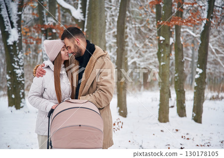 Parents with pram. Lovely couple have a walk in the winter forest Parents with pram. Lovely couple have a walk in the winter forest 130178105
